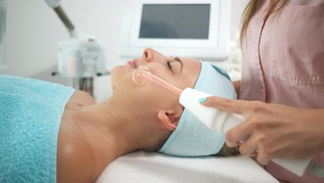Beautician therapist applying face treatment in beauty salon to young woman.