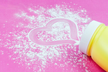 Children's concept. Scattered baby powder with a heart-shaped pattern in a yellow bottle on a bright pink background.