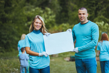 Naklejka premium A couple holding a poster in their hands and showing it to the camera, posing standing in nature, smiling at the camera.