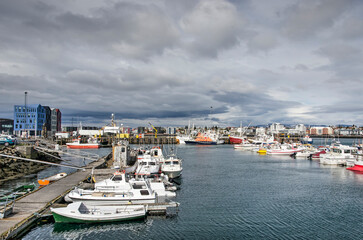 Fototapeta na wymiar Hafnarfjörður, Iceland, May 8, 2022: boats in the town's harbour lit by the sun with a cloudy sky