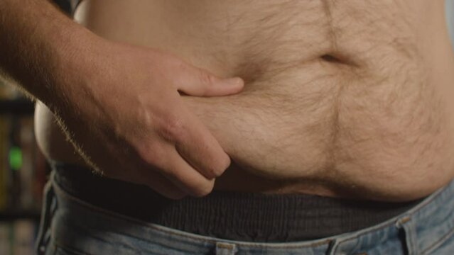 Close up of Shirtless man grabbing belly fat and grabbing love handle - front view
