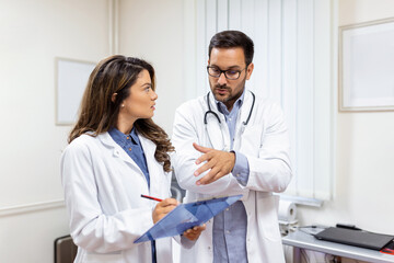 Doctors discussing over a medical report in hospital. Female and male doctor checking clinical report of patient online. Healthcare staff having discussion in a office of private clinic.