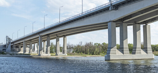 Support pillars of highway bridge over river. Industrial background