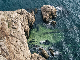 Top aerial view of blue sea water and rocky cliff