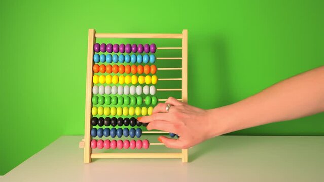 Female hand slowly counts on a children's wooden abacus. Close-up of flipping wooden circles. Counting on a children's account.