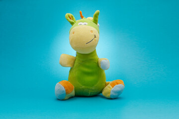 Cute plush dragon siting isolated on blue background.