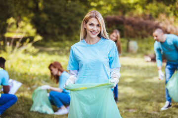 A group of creative young volunteers collect garbage in the open in a public park. Portrait of a young beautiful girl holding a garbage bag