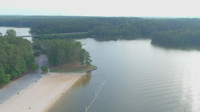 aerial footage of the rippling green waters of Lake Acworth surrounded by lush green trees, grass and plants with a beach on the banks of the lake at Proctor Landing Park at Lake Acworth in Acworth 