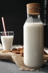 Glass bottle of milk and cookies on dark background