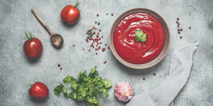 Homemade tomato sauce in a bowl with spices, fresh tomatoes and greens, gray concrete grunge background. Top view, banner, toned image.