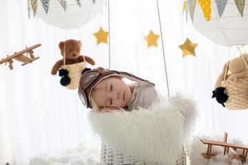 Sweet toddler boy, playing with airplane and teddy bear, air balloons with toys behind him