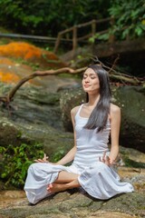 Asian young female lady yoga model meditate and practicing yoga zen poses in a nice, quiet tranquil green outdoor forest park with giant stone, tree and nice little stream waterfall
