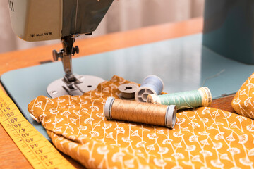 still life with tailor material including thread reels, tape measure, sewing machine and orange fabric