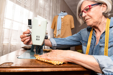 close-up of an elderly woman manipulating a sewing machine, in the background a mannequin dressed in an orange blouse