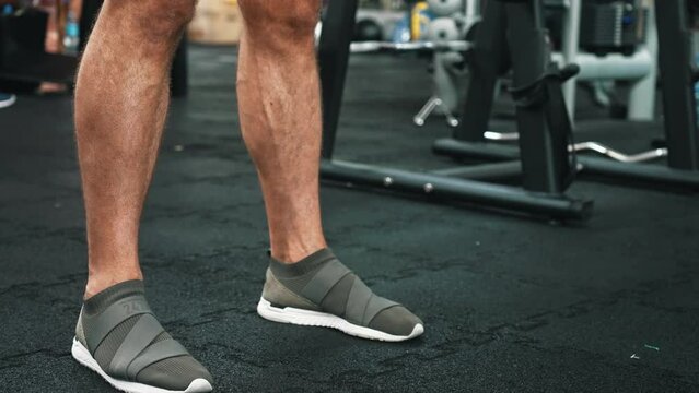 Closeup portrait of legs of a caucasian person in sports shoes lifting the weight bar. Gym interior. Strength concept. High quality 4k footage
