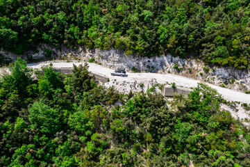 Aerial of Offroad truck driving on a narrow mountain road through the forest