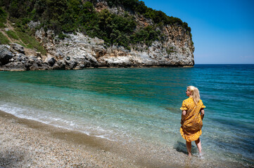 Blonde girl in yellow dress standing at Fakistra beach on pelion peninsula in Greece