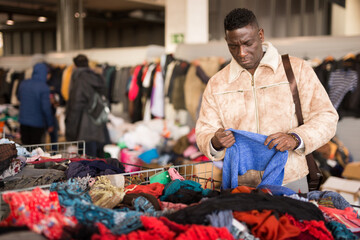 african american guy chooses sacond hands clothes at flea market