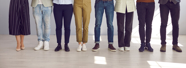 Cropped image of legs of different men and women standing in row in bright room. Unknown men and...