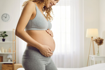 Crop shot of smiling sporty healthy young woman touch caress belly excited with pregnancy await for baby birth. Happy pregnant woman enjoy maternity leave. Motherhood and parenting. - obrazy, fototapety, plakaty