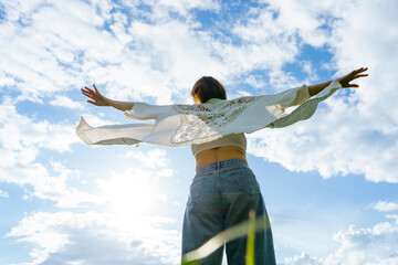 a young girl in a boho cape against the blue sky spread her arms like a pilot