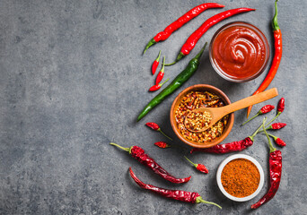 Chili spicy condiment in bowl and fresh chili peppers and dry flakes spices on dark background copy space. 