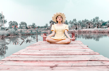 Woman practicing yoga and meditating in lotus position on wooden bridge.