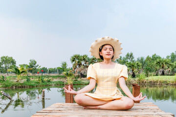 Woman practicing yoga and meditating in lotus position on wooden bridge.