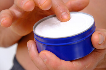 close-up of man smears nivea for men cream from new large round blue jar, skin care cosmetic,...