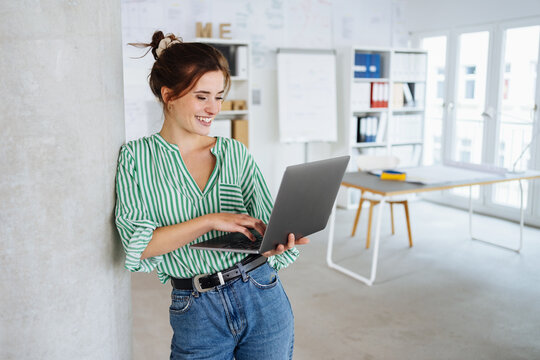 Happy young business woman standing with her laptop in office