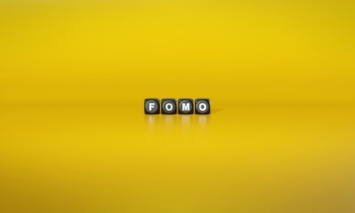 Acronym ‘FOMO’ or ‘Fear of Missing Out’ spelled out in white text on dark wooden blocks against plain yellow background. 3D rendering