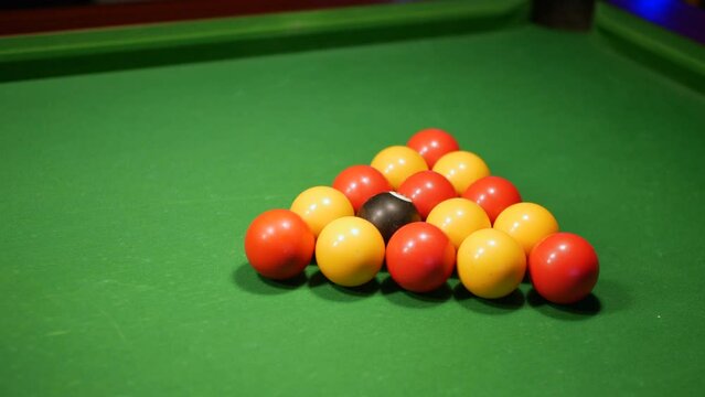 A man setting up the pool balls on a table in a triangle. He spins the eight ball