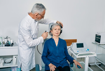 Obraz premium Senior woman while tympanometry or impedance audiometry and test of middle-ear function with ENT-doctor using tympanometer probe at hearing center