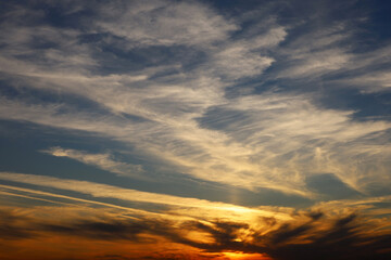 Sunset on a blue sky, sun is shining through the dark and orange clouds. Picturesque landscape for background with soft colors