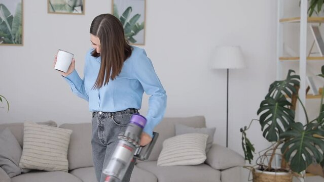 Charming brunette housewife enjoying time at home while cleaning carpet with modern vacuum. Concept of housekeeping.