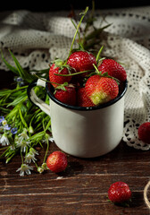 Garden strawberries in a cup, on a lace napkin, on a dark wooden table with a bouquet of wildflowers