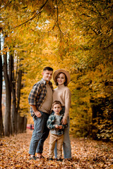 Fototapeta premium Portrait of happy young family on the background of autumn park. Mom, dad and son are smiling. Family autumn photo shoot