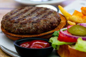 Fast food. selective focus of hamburger with ingredients. Side view with copy space for your text.  Hearty Grilled Hamburger with Lettuce, ketchup, mayonnaise, fries, salad and tomato. Junk food.