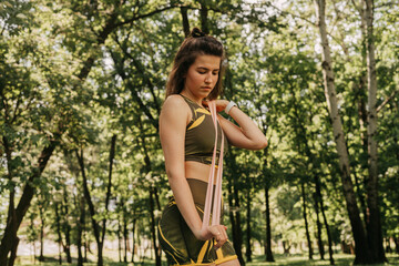 a young girl goes in for sports with elastic for fitness in the park / in the forest. in a green suit on a yoga mat