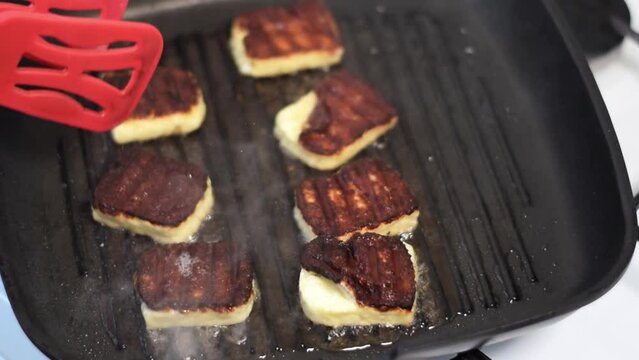 Grilling halloumi cheese on grill pan in the kitchen. Turning the slices with golden crust. Zoom in