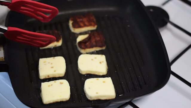 Grilling halloumi cheese on the grill pan in the kitchen. Turning the slices with golden crust