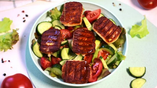 Grilled halloumi cheese is dressed with olive oil on vegetable salad with tomato, cucumber and lettuce on the plate. Serving appetizer