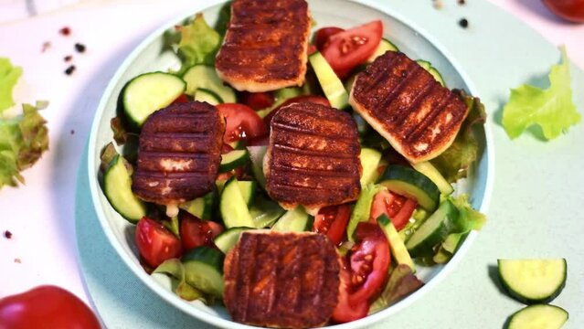 Grilled halloumi cheese is dressed with olive oil on vegetable salad with tomato, cucumber and lettuce on the plate. Serving appetizer