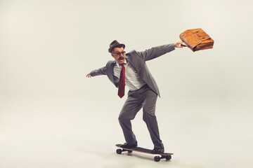Young funny man, businessman dressed in suit in 50s, 60s fashion style rides skateboard isolated on...