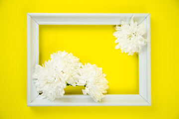 A white frame with three white flowers on a bright yellow background inside. High quality photo
