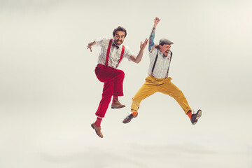 Fototapeta na wymiar Two cheerfull dudes, young men in old-school fashioned attire running, jumping, having fun isolated on white background. Vintage, retro style concept