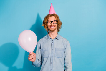Photo of funky cute young guy dressed jeans shirt eyewear headwear holding balloon isolated blue...