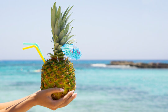 Fresh Pineapple  drink coctail on woman hand at tropical beach and sea background with copy space . Tropical summer concept  card