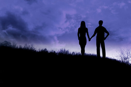 silhouette of a couple hand in hand at evening along a ridge