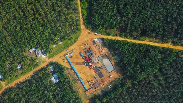 Cinematic Onshore Drilling and Workover Rig structure and Rig equipment for oil exploration and exploitation in the middle of jungle surrounded by palm oil trees during sunset time.